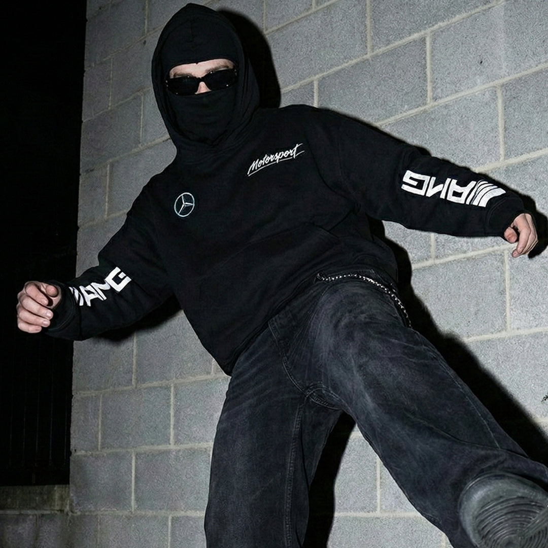 Model wearing oversized Mercedes-AMG streetwear hoodie with baggy jeans and balaclava.
